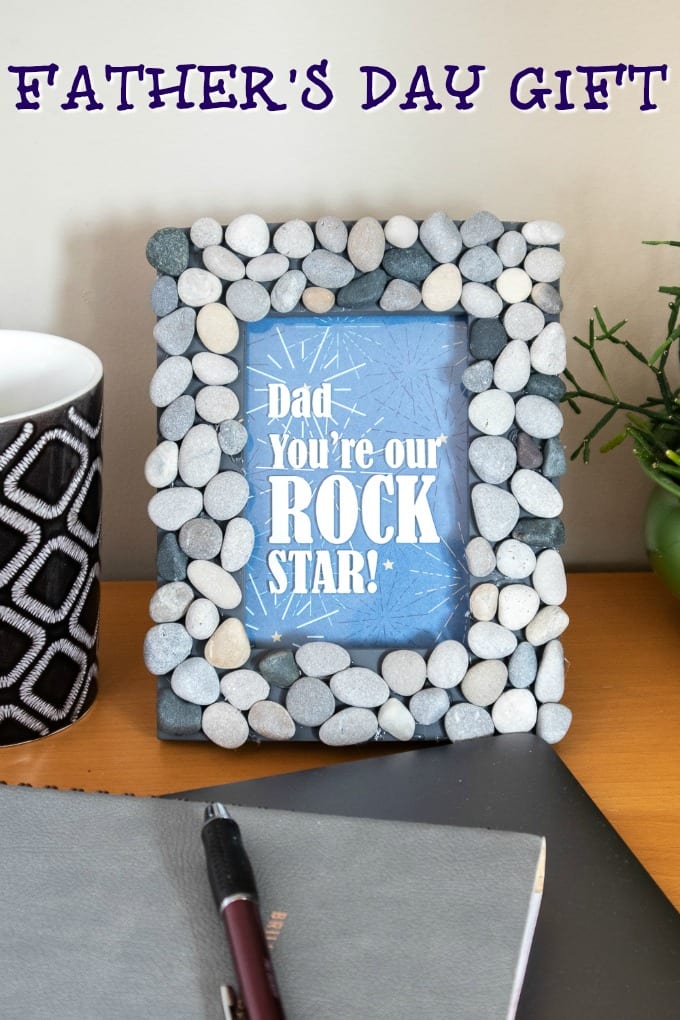 Image of a picture frame covered in small rocks sitting on a desk top. The frame contains the phrase Dad You're Our Rock Star!
