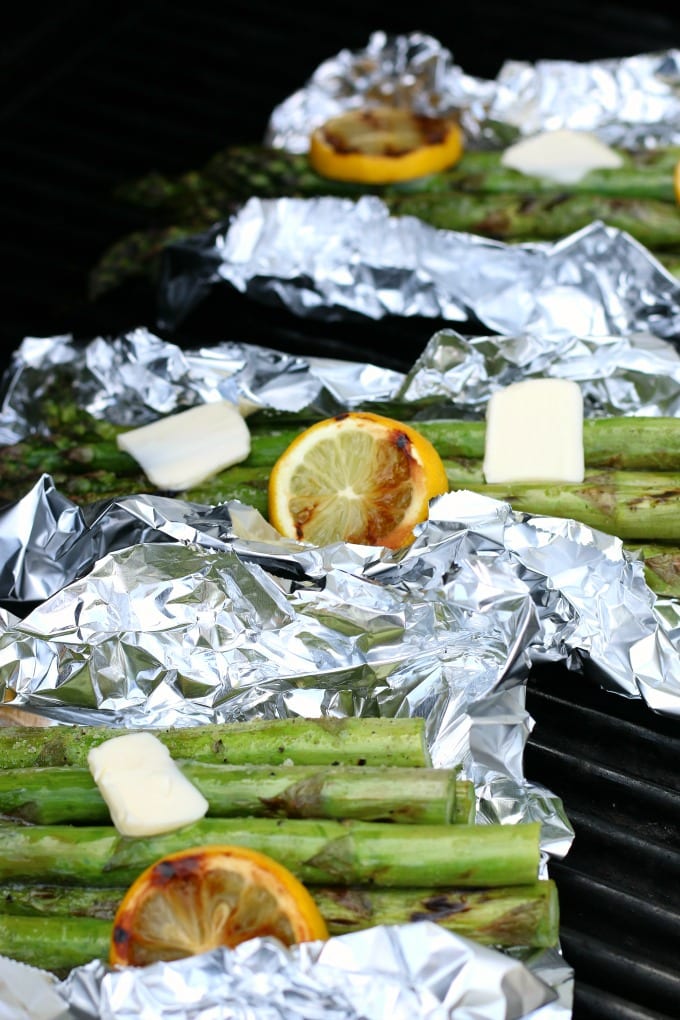 Grilled Asparagus Recipe - foil packets of grilled asparagus, grilled lemons and butter are shown on the grill.