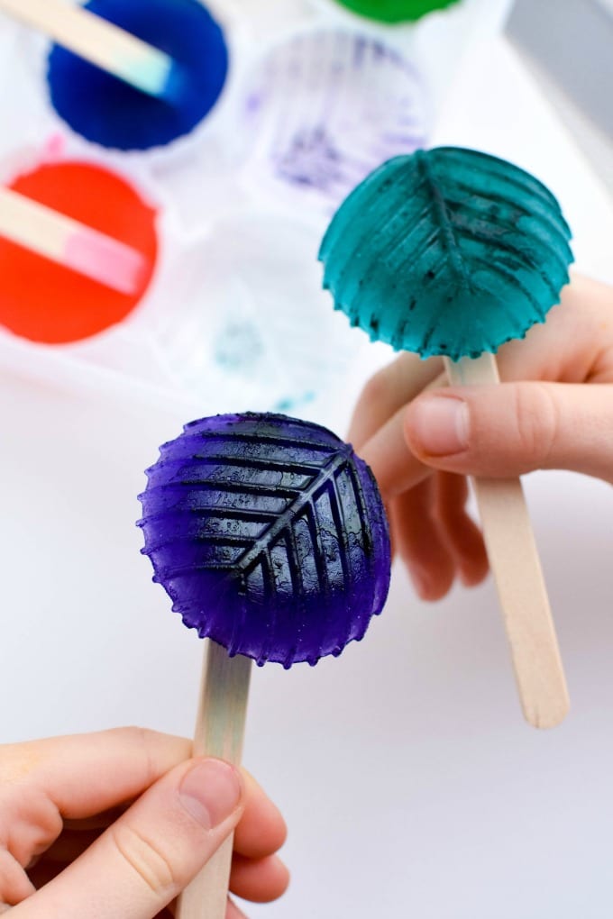 Ice Cube Painting - Child's hands holding an frozen water dyed with food coloring on craft sticks.