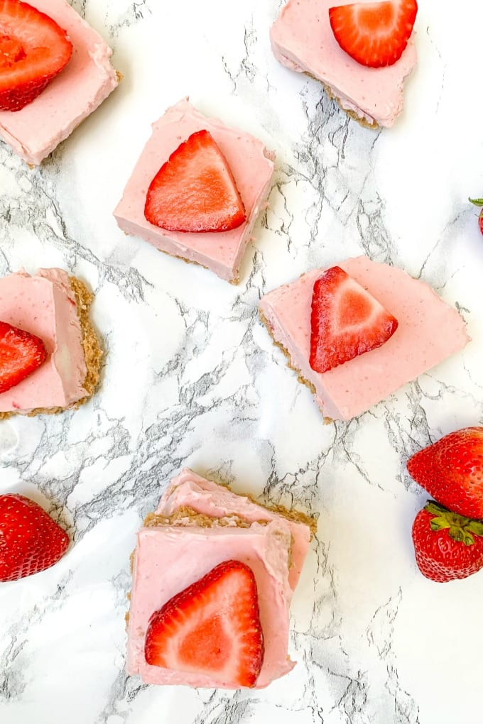 Sliced no bake strawberry cheesecake bars on a marble counter top.
