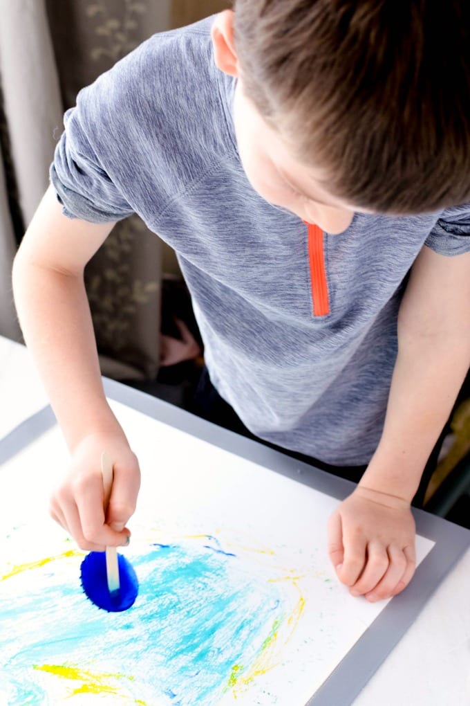 Painting with Ice Cubes - a young boy paints with a blue ice cube on a craft stick.