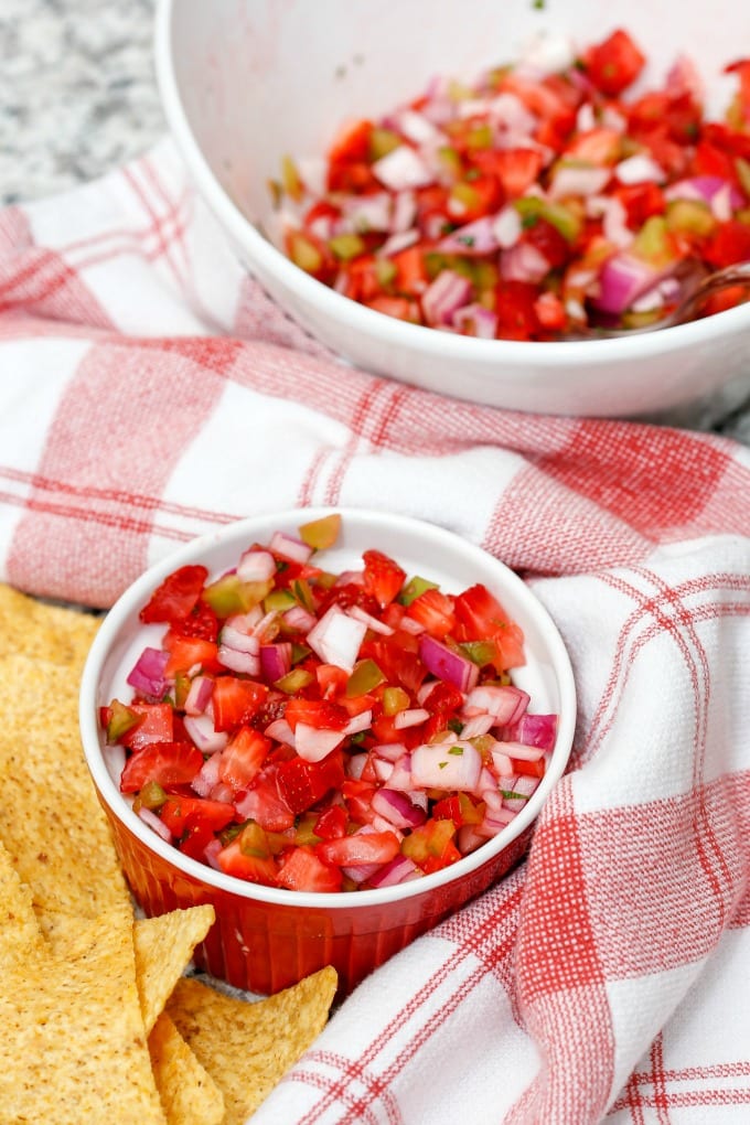Strawberry salsa in a red ramekin, accompanied by a red and white towel and tortilla chips.