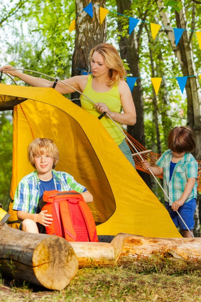 backyard camping ideas - mom and two boys setting up a yellow tent for camping
