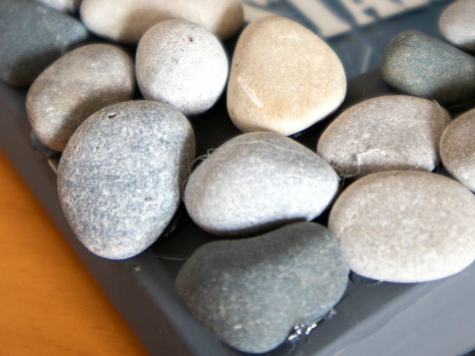 Image contains a close up of small rocks hot glued to a gray painted picture frame.