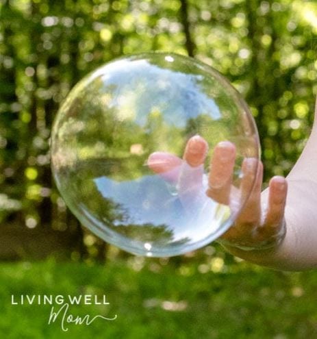 Large bubble sitting on the fingertip of a child.