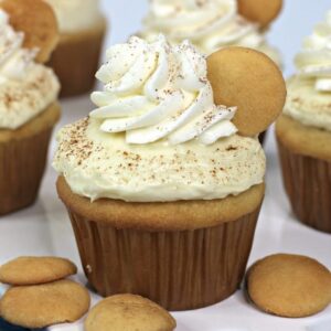 Square, close up image of a banana pudding cupcake on a white platter with NIlla wafers.