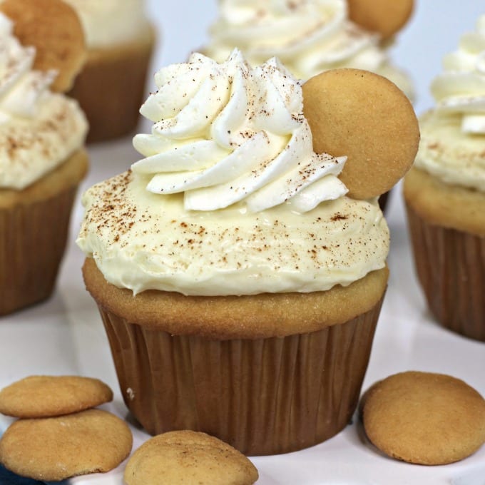 Square, close up image of a banana pudding cupcake on a white platter with NIlla wafers.
