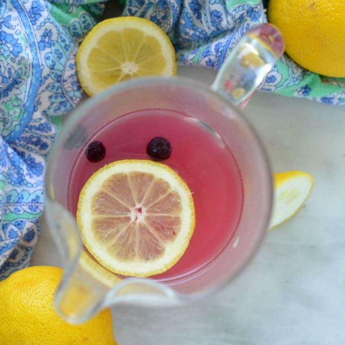 A birds eye view of a blueberry lemonade recipe in a glass pitcher. Topped with a fresh lemon slice and blueberries.