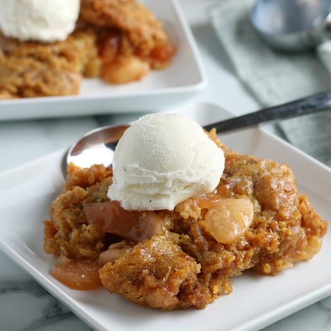 Square, close up image of slow cooker apple cobbler on a white plate.