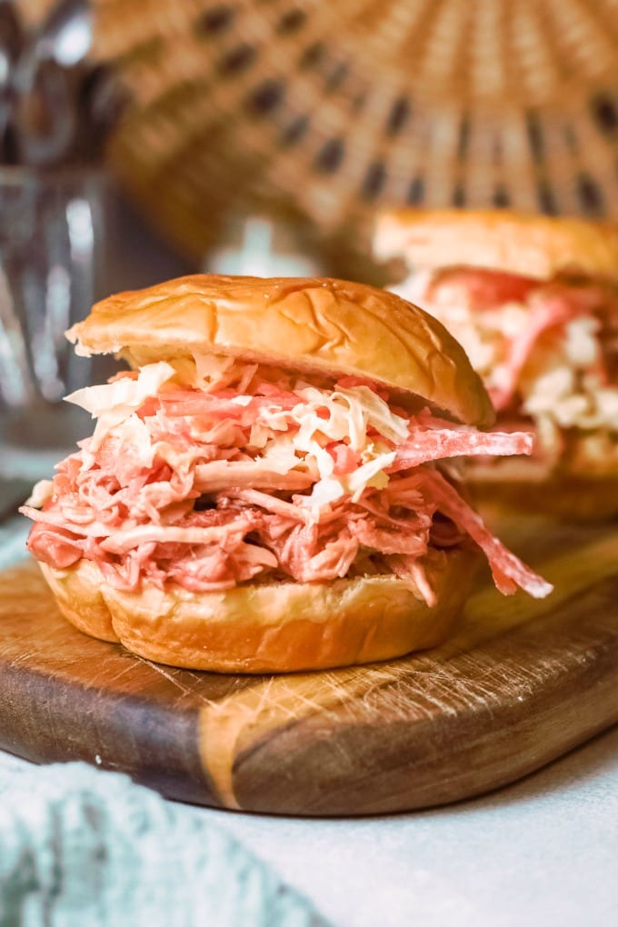 Close up image of a pulled bbq chicken sandwich on a wood cutting board. 