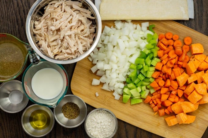 Chopped vegetables on a cutting board alongside a bowl of shredded rotisserie chicken.