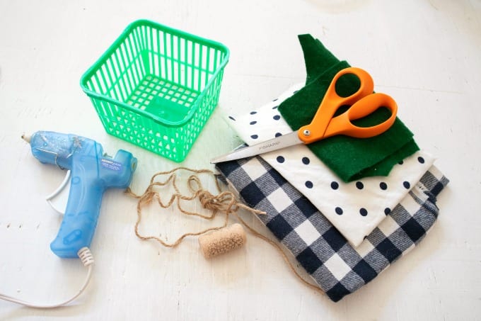 Image contains the materials needed to make a scrap fabric pumpkin - hot glue gun, cork, twine, empty strawberry basket, felt, scissors and scrap fabric.
