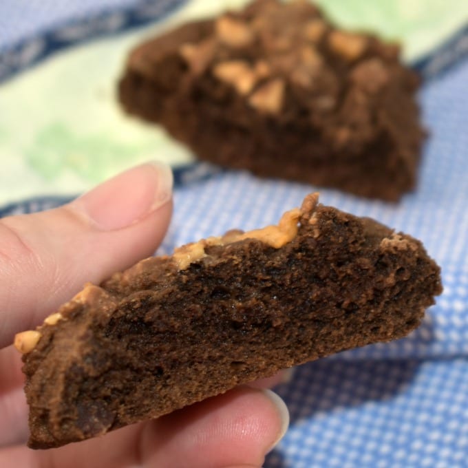 Hand holding half of a double chocolate toffee cookie.