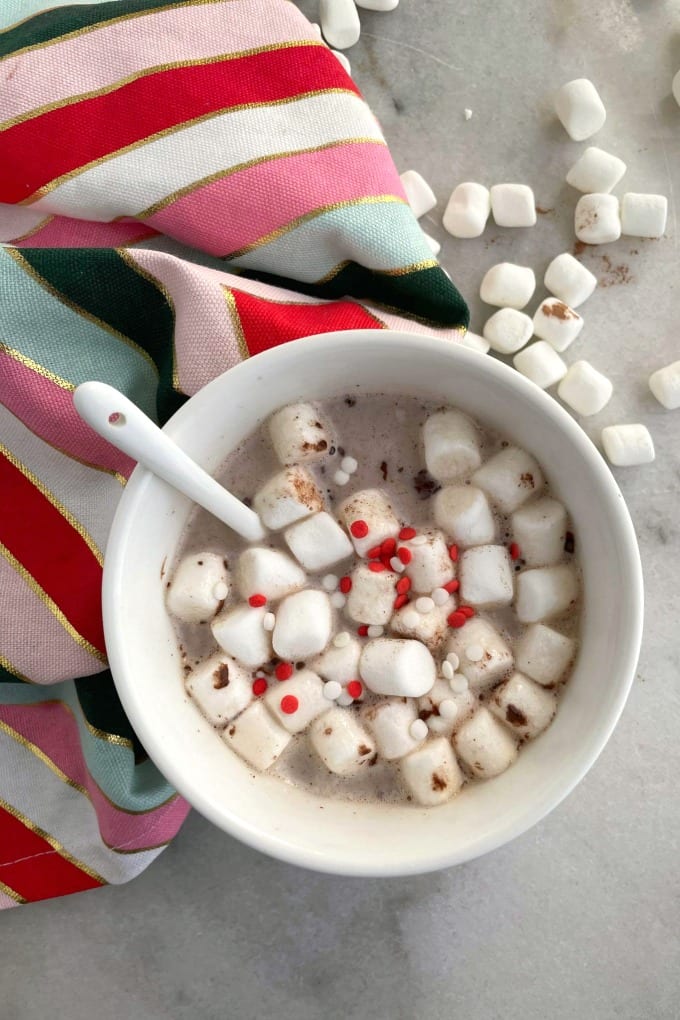 Hot chocolate in a white mug and topped with mini marshmallows and sprinkles. 