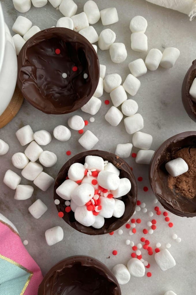 Birds eye view of halved hot chocolate bombs filled with and surrounded by sprinkles and mini marshmallows. 