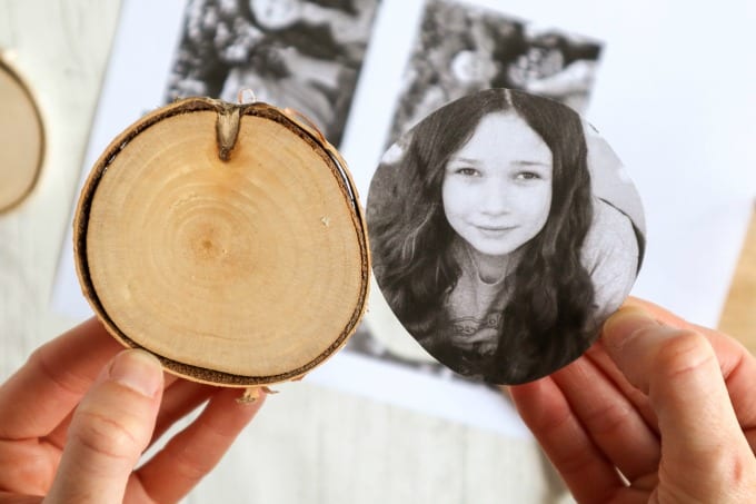 A hand holds a wood slice with a sized photo to be made into an ornament.