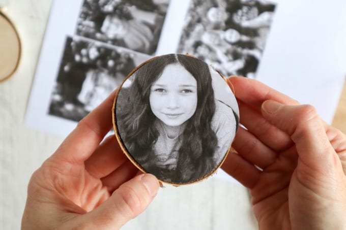 A hand holds a wood slice with a sized photo to be made into an ornament.