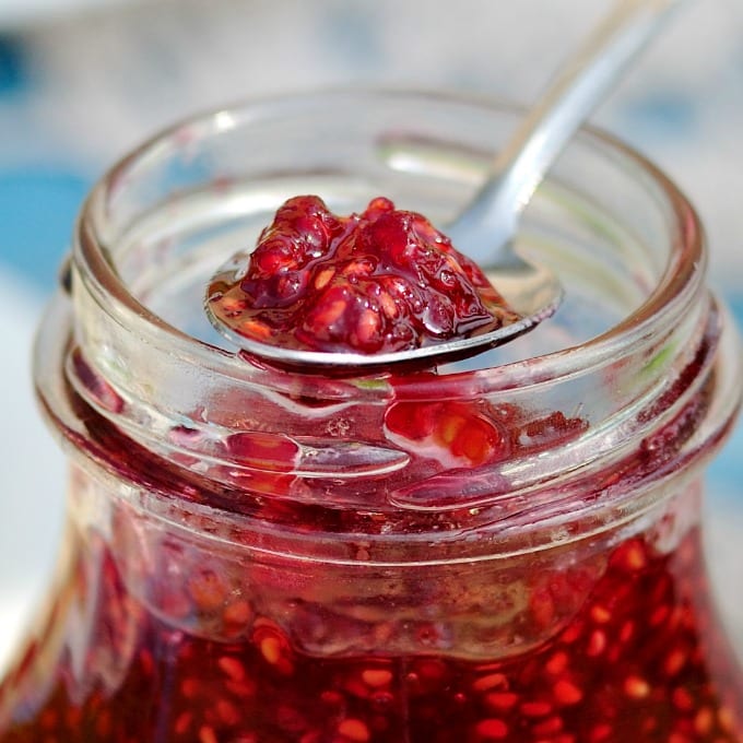 close up of a jar of a jar and a spoon with raspberry jam.