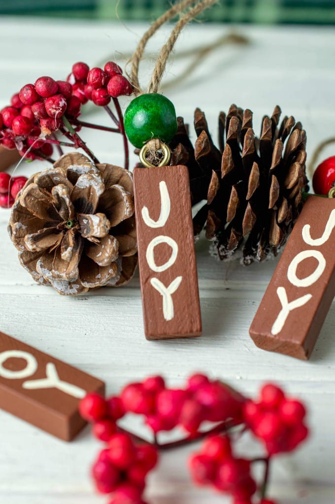 Painted wood ornaments that say Joy surrounded by Christmas greenery and pine cones.