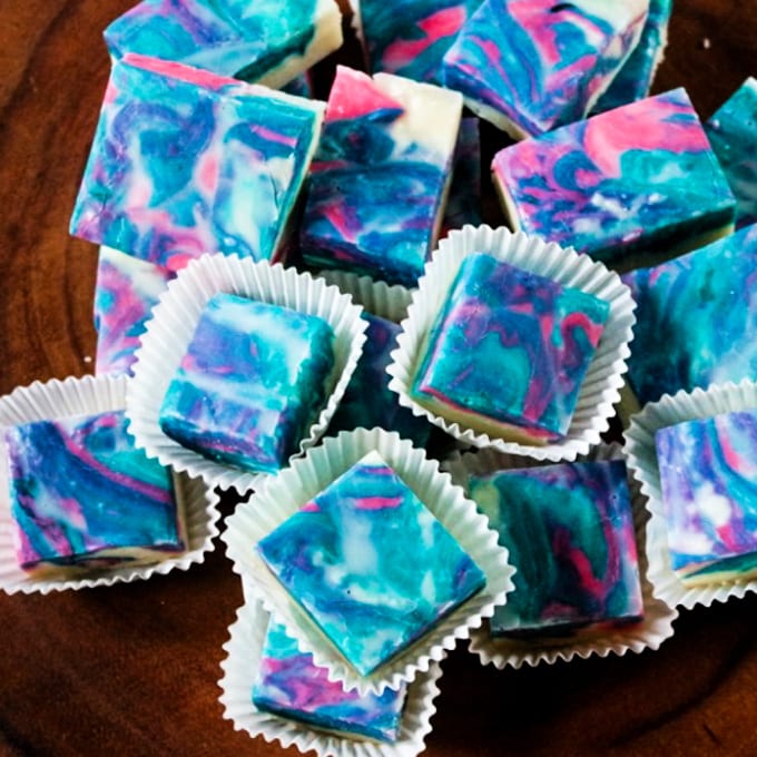 close up of cotton candy fudge in paper wrappers on a wooden pedestal