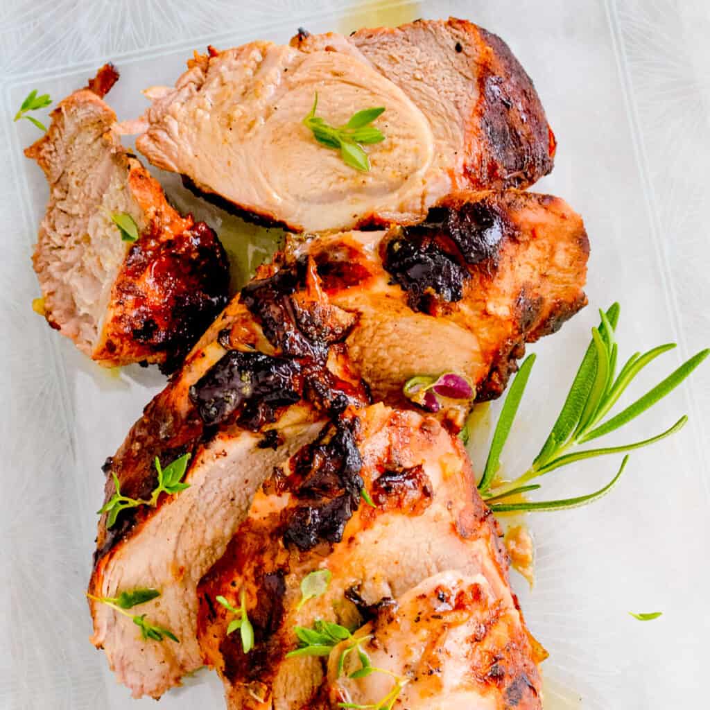 Close up image of pork loin topped with herb butter and fresh herbs.