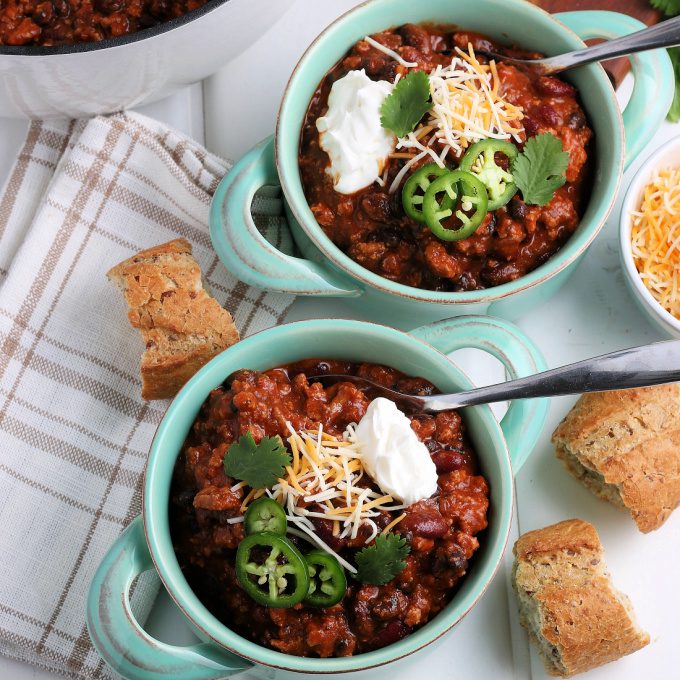 Two bowls of leftover turkey chili surrounded by a large pot filled with chili and fresh bread.