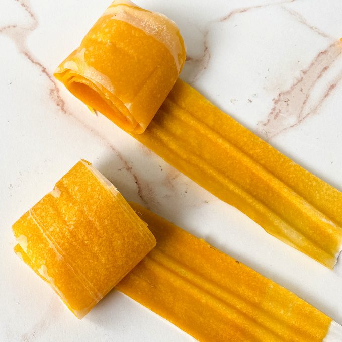 Two rolls of mango fruit leather on a white countertop.