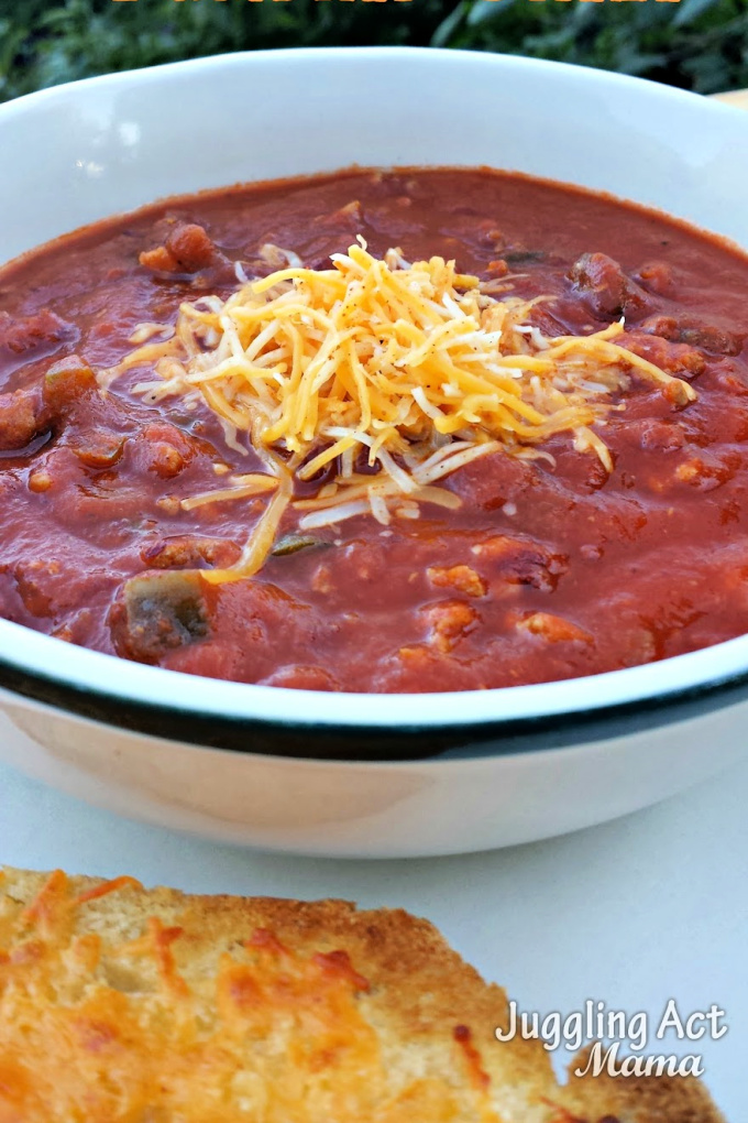 Close up image of a bowl of pumpkin chicken chili topped with shredded cheese and cheesy bread on the side.