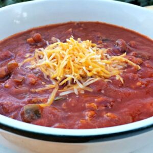 Close up image of pumpkin chicken chili in a white bowl, topped with cheese.