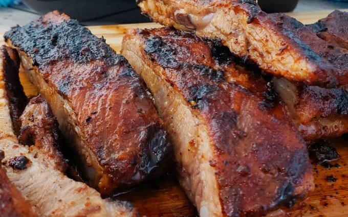 Grilled pork ribs are sliced on a cutting board with a bottle of merlot in the background.