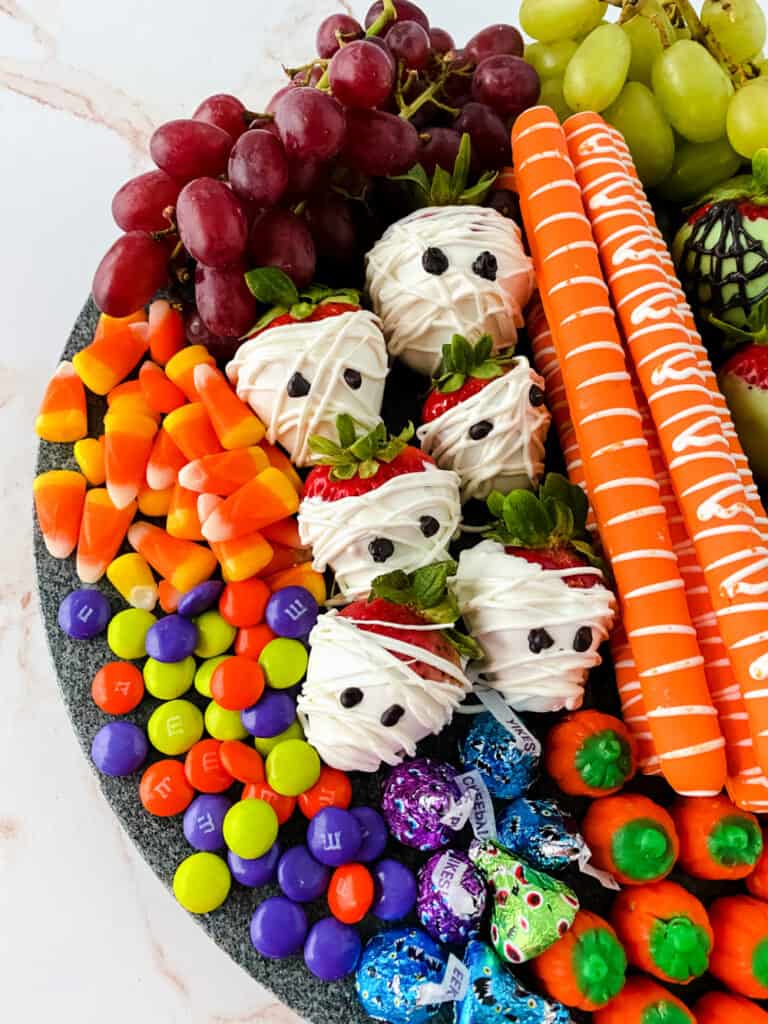 Top down view of candy, fruit, and chocolate-covered strawberries and pretzels on a snack board. 