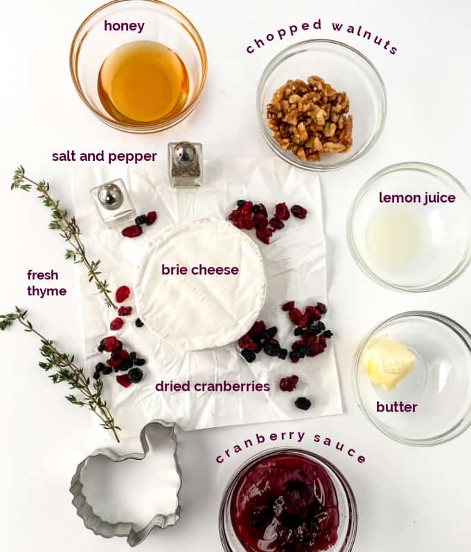 Image contains ingredients you need to make baked brie with cranberry sauce - honey chopped walnuts, salt and pepper, lemon juice, brie cheese, fresh thyme, dried cranberries, cranberry sauce and butter. 