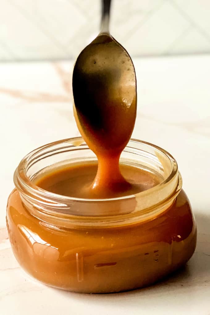 Homemade caramel sauce pouring from a spoon, into a small glass mason jar.