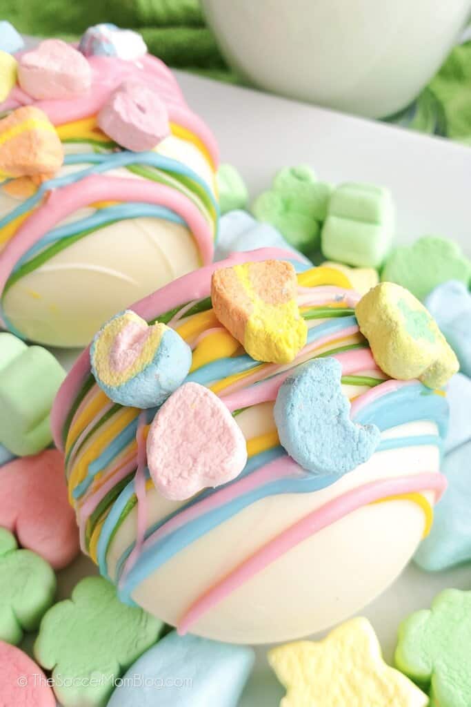 A white plate filled with Lucky Charms marshmallows, topped with Lucky Charms Hot Cocoa Bombs.