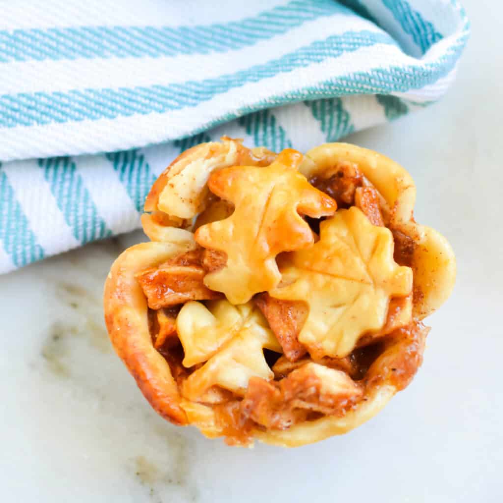 Square, close up image of a mini apple tart next to a clean kitchen towel.