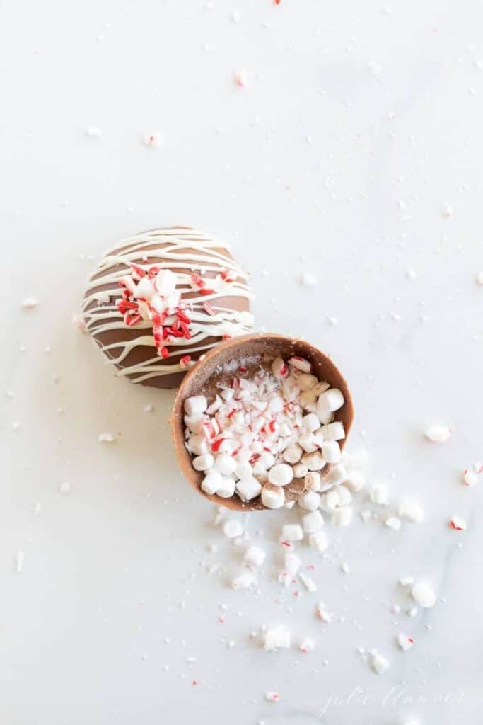Top down image of peppermint hot chocolate bombs. One is cut in half and mini marshmallows and peppermint bits are spilling out.
