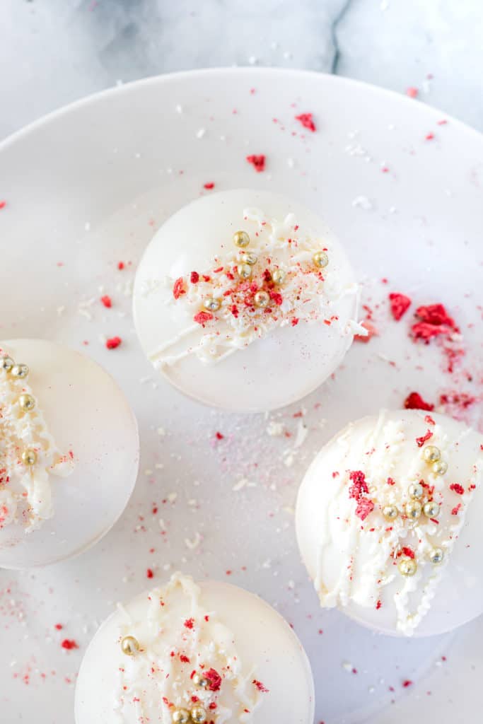 Strawberry White Hot Chocolate Bombs topped with freeze tried strawberries and gold non-pareils. 
