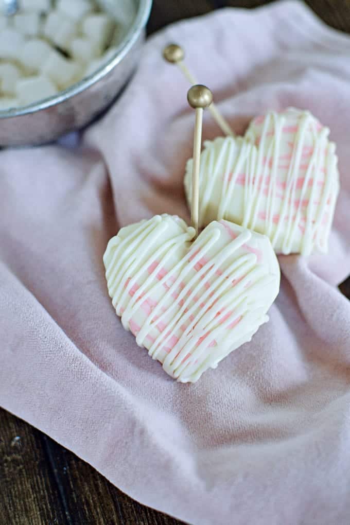 Close up image of heart-shaped, white chocolate hot cocoa bombs on a pink cloth.