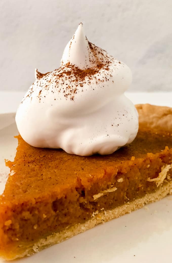 Close up image of a sweet potato pie slice topped with whipped cream.