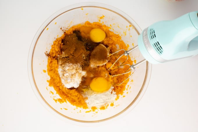Top down image of a glass mixing bowl filled with ingredients along with a handmixer.