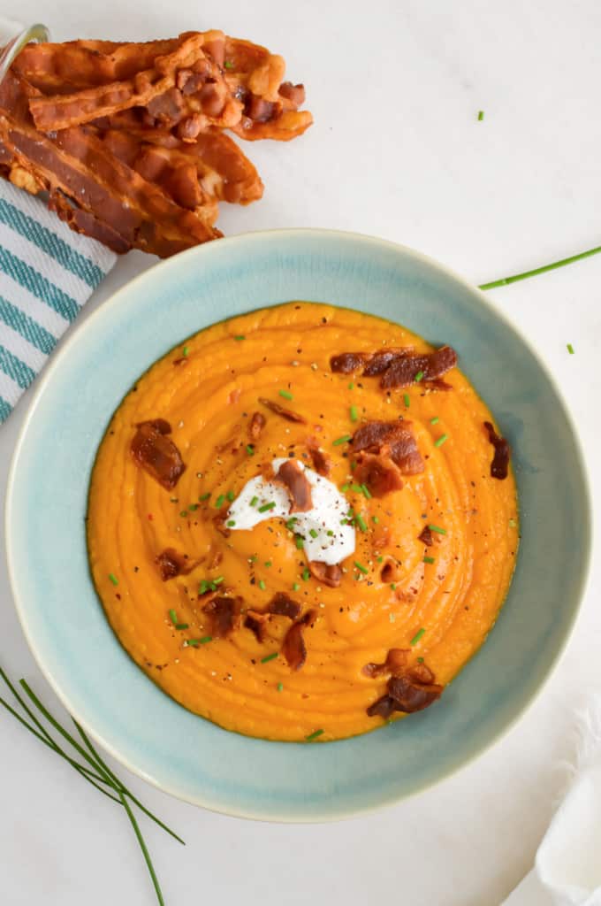Top down view of sweet potato soup in a blue bowl, topped with bacon and sour cream.