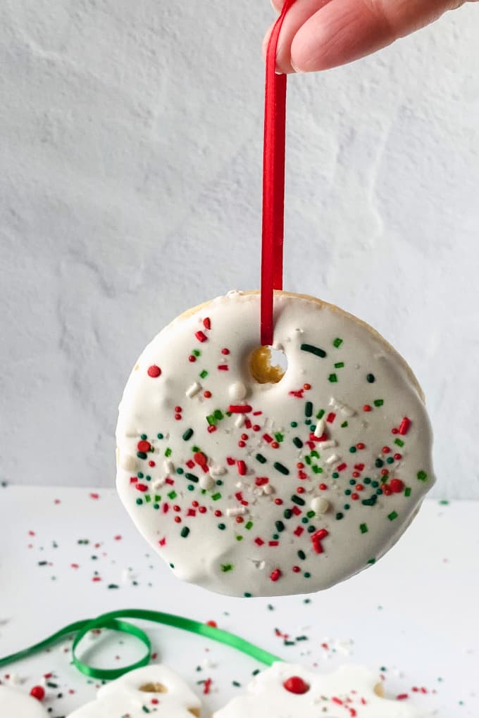 Round ornament sugar cookie topped with royal icing and sprinkles, hanging from a red ribbon.
