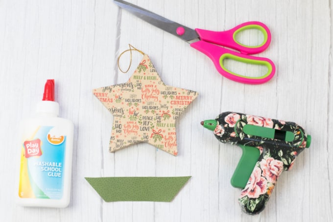 Image contains glue, scissors, a hot glue gun, a paper mache ornament covered in scrapbook paper and a strip of scrapbook paper.