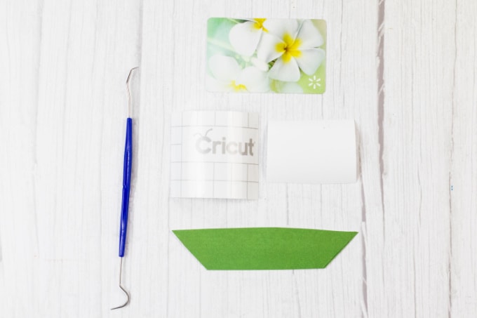Image contains a weeding tool, scrapbook paper strip, transfer tape and a vinyl word waiting to be weeded.