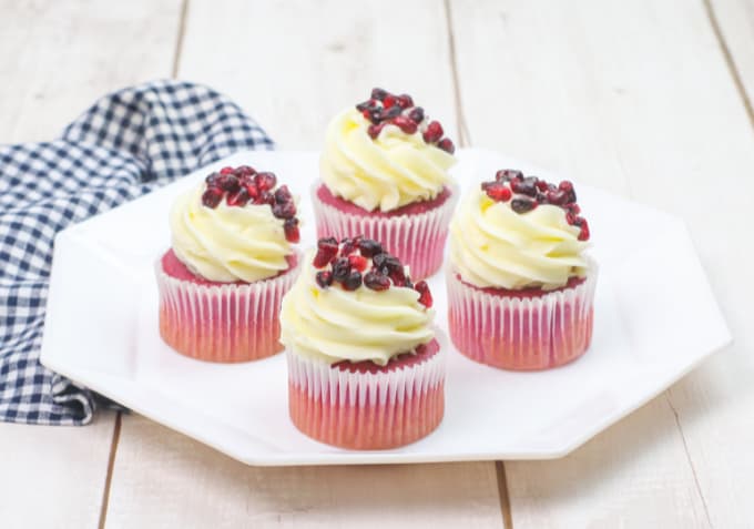 Four pomegranate cupcakes on a white octagonal plate with a blue checked napkin.