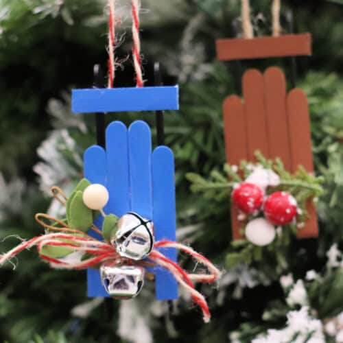 Close up image of a popsicle stick sled ornament on a Christmas tree with another in the background.