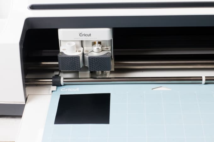 Close up image of a Cricut cutter cutting words out of black vinyl.