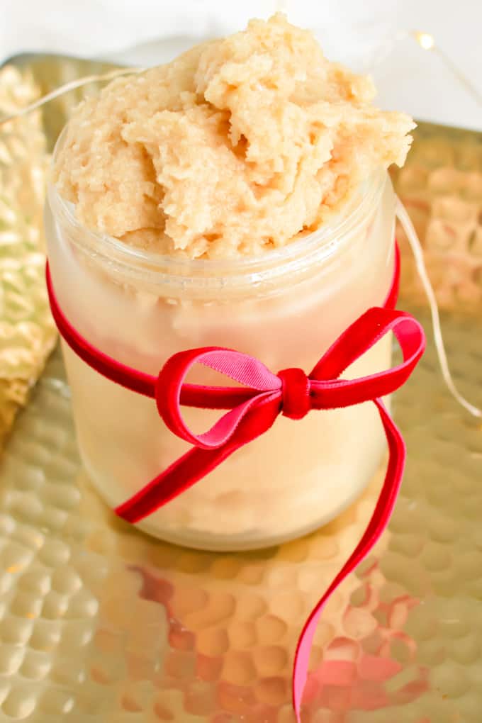 Close up image of coconut oil sugar scrub in a small jar with a red ribbon.