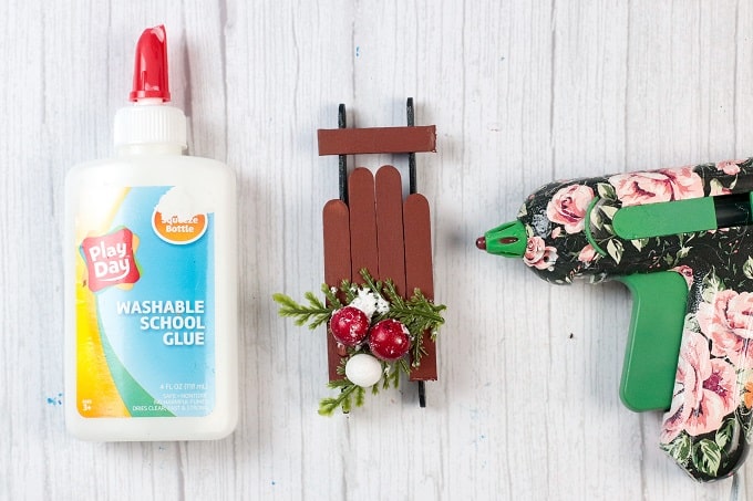 Image contains a glue gun, a bottle of glue, and a popsicle stick sled ornament.