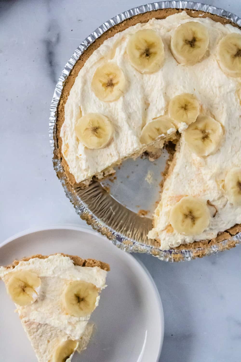 Top down view of a Banana Pudding Pie with a slice removed to a plate next to it.